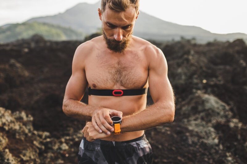 Athletic man watching training results on smart watch or fitness tracker. Running topless and using chest heart rate monitor. Body close-up.