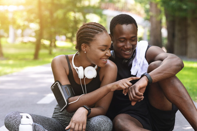 Curious Black Couple Using Smartwatch Fitness Tracker After Outdoor Workout, Checking Burned Calories